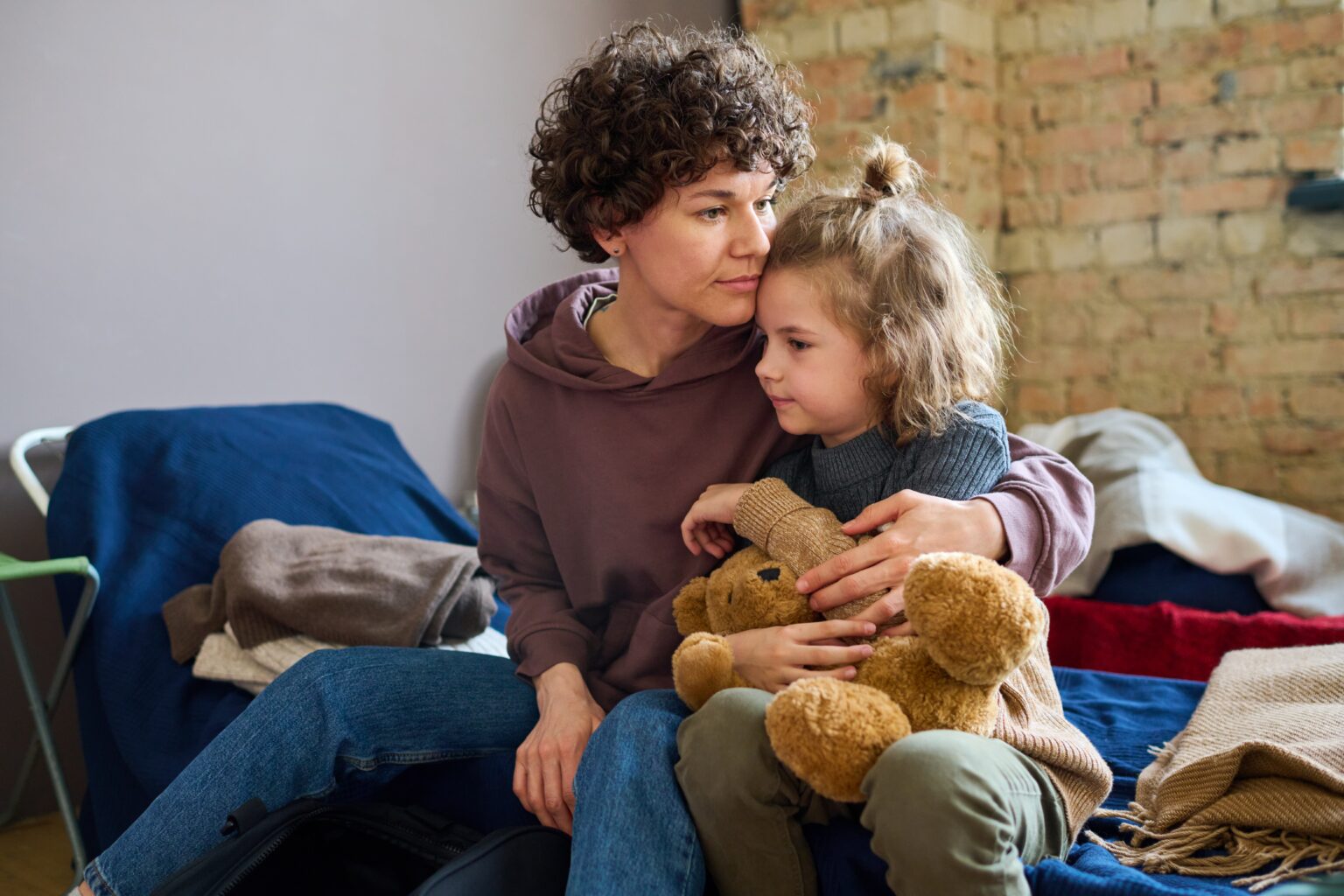 A mother comforting her daughter holding a toy bear in a living room.